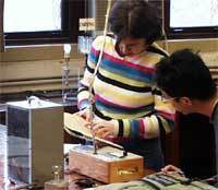 a pair of students look at a notebook over a cluttered workbench
